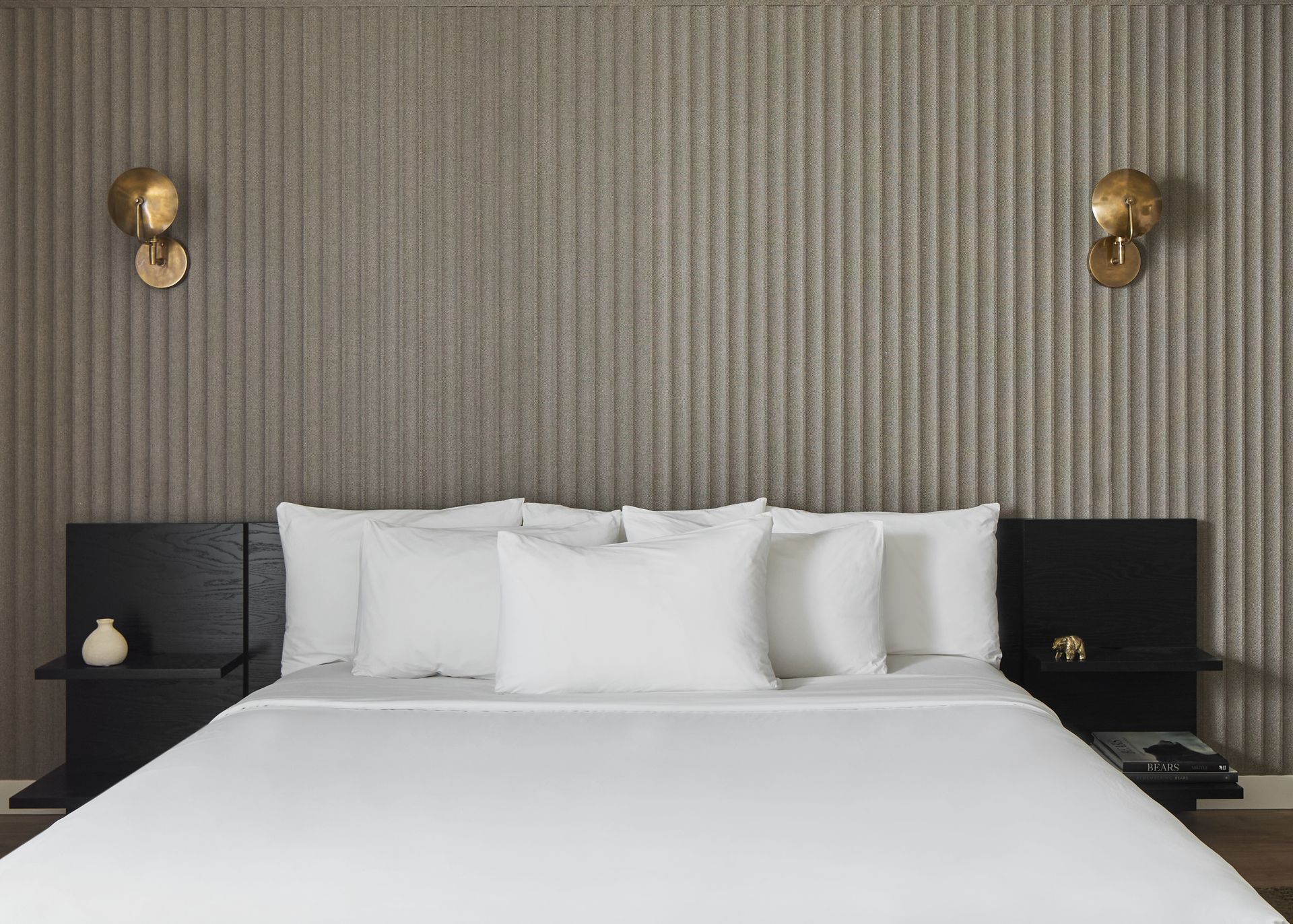 Modern bedroom with a neatly made white bed, dark bedside tables, and brass wall sconces on striped wallpaper