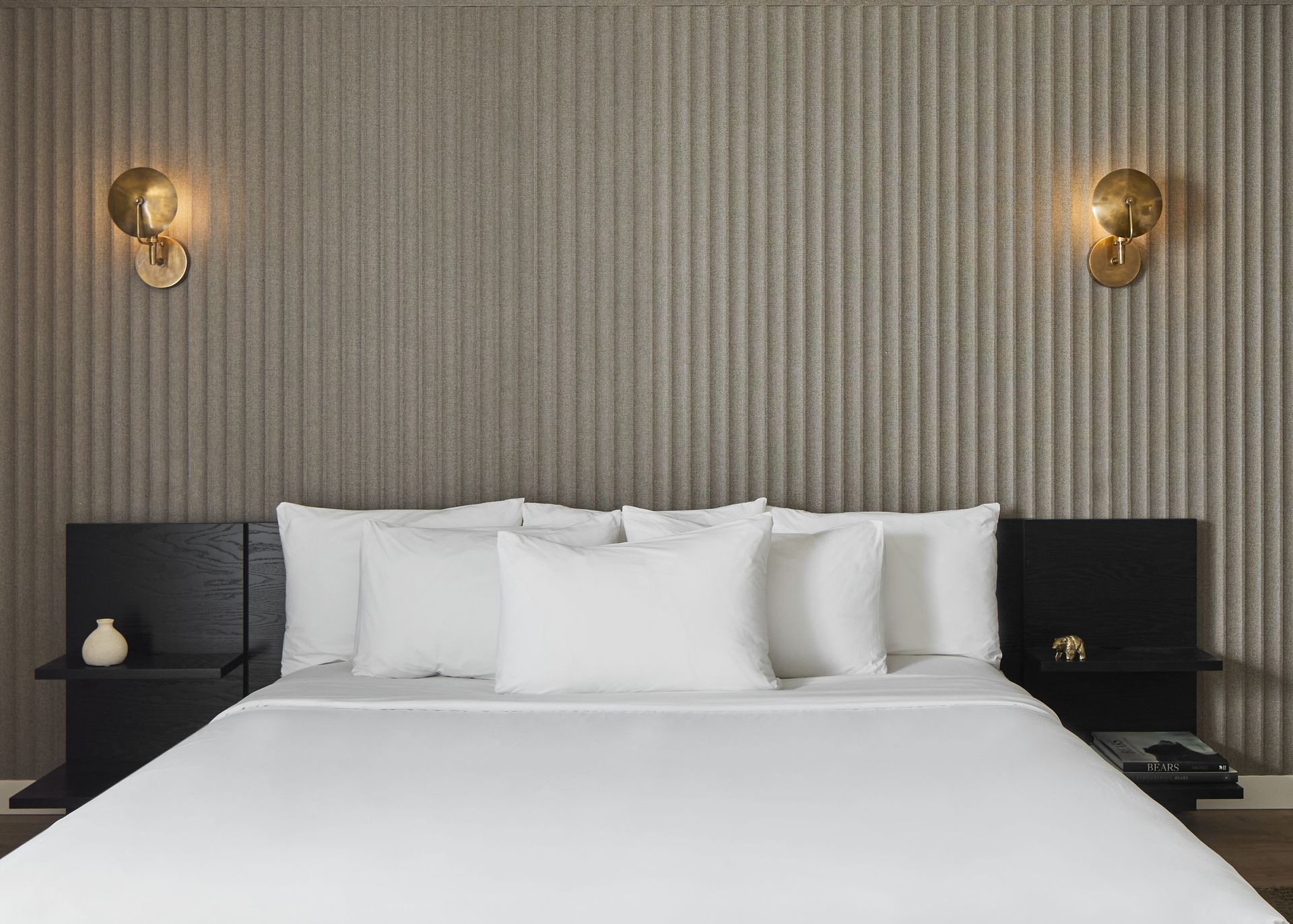 Modern bedroom with a white bed, black nightstands, and wall sconces against a textured beige wall