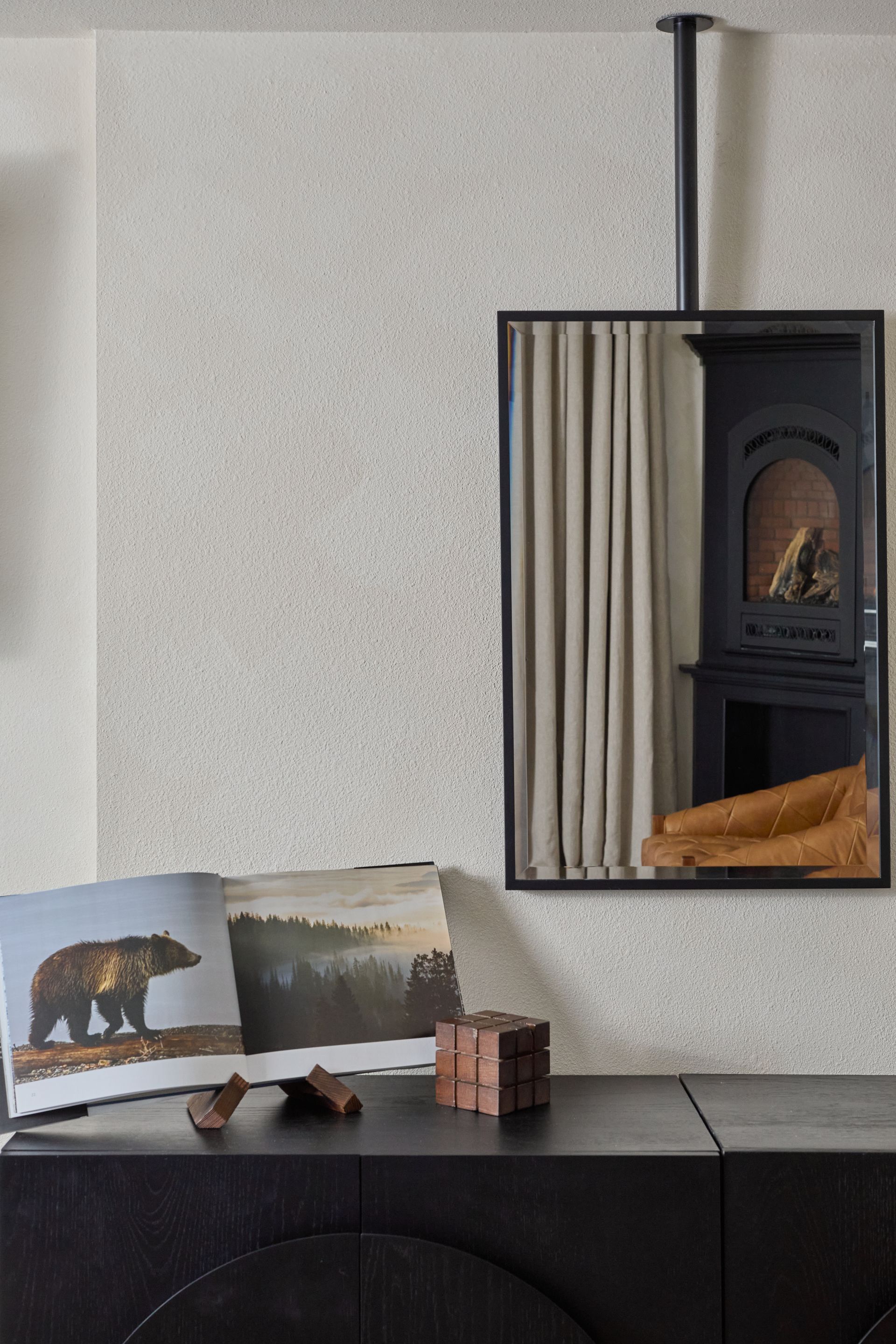 Small shelf with an open photo book, bear picture, and a mirrored reflection of a fireplace in a minimalist room