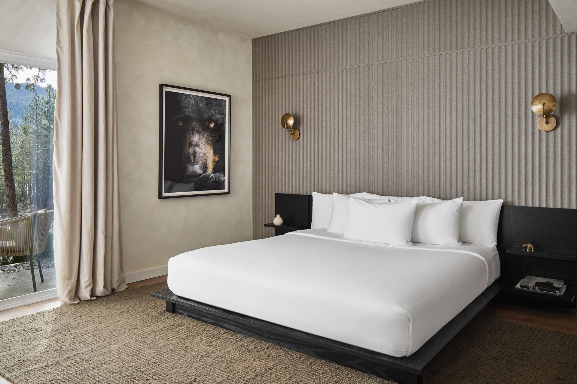Modern bedroom with a large white bed, textured wall, framed art, and sliding glass door to a balcony