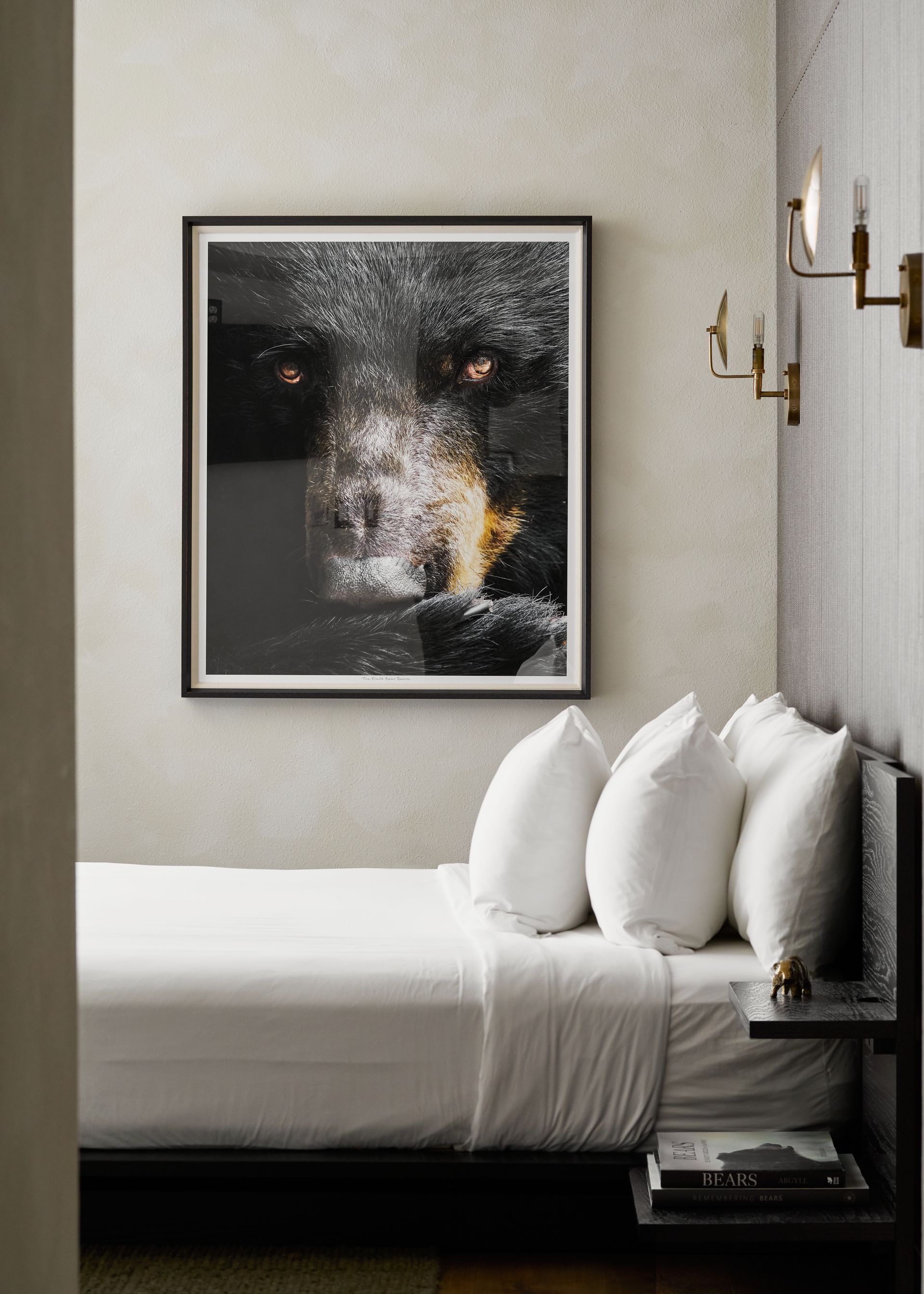 Minimal bedroom with a white bed, black-framed abstract art, and wall-mounted brass lights