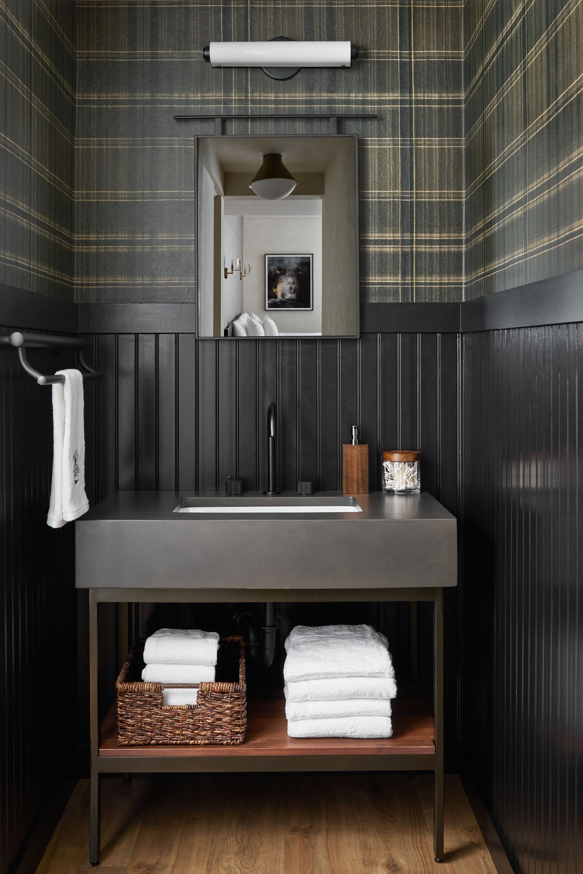 Modern black-and-gray bathroom vanity with mirror, sink, folded white towels, and woven baskets underneath