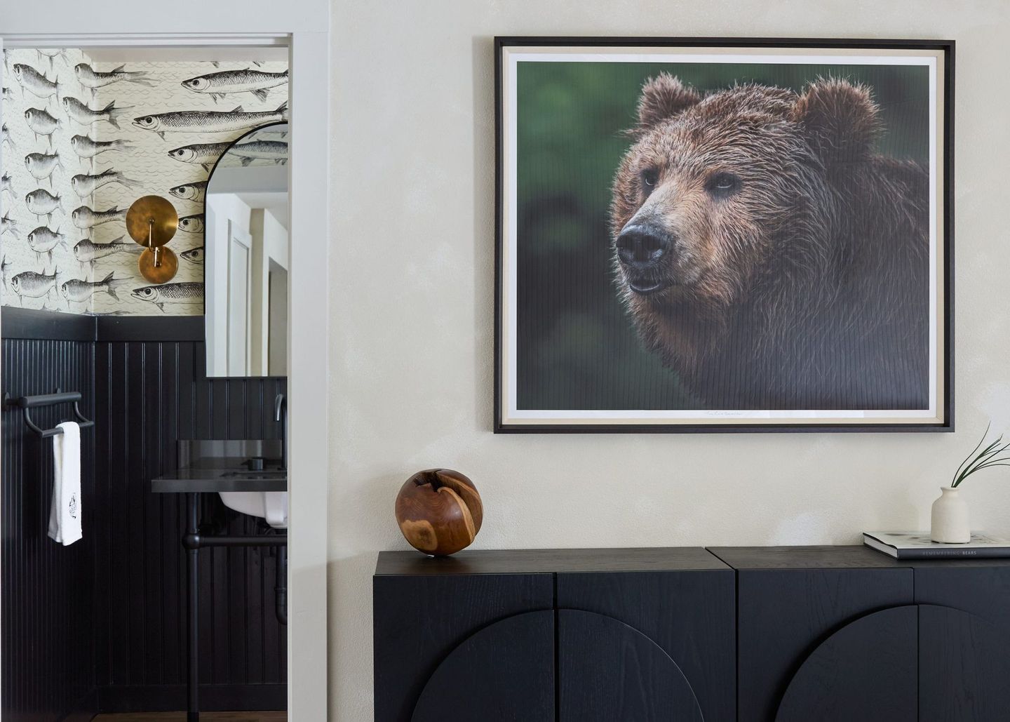 Framed bear portrait above a black cabinet in a modern room with white walls and dark wood accents