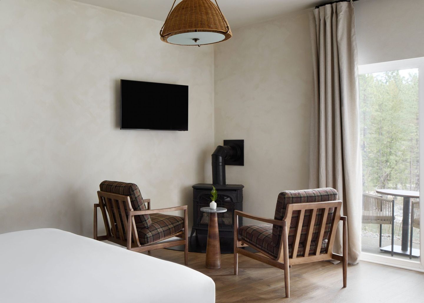 Modern hotel bedroom with wall-mounted TV, two chairs, small table, and sliding glass door to balcony.