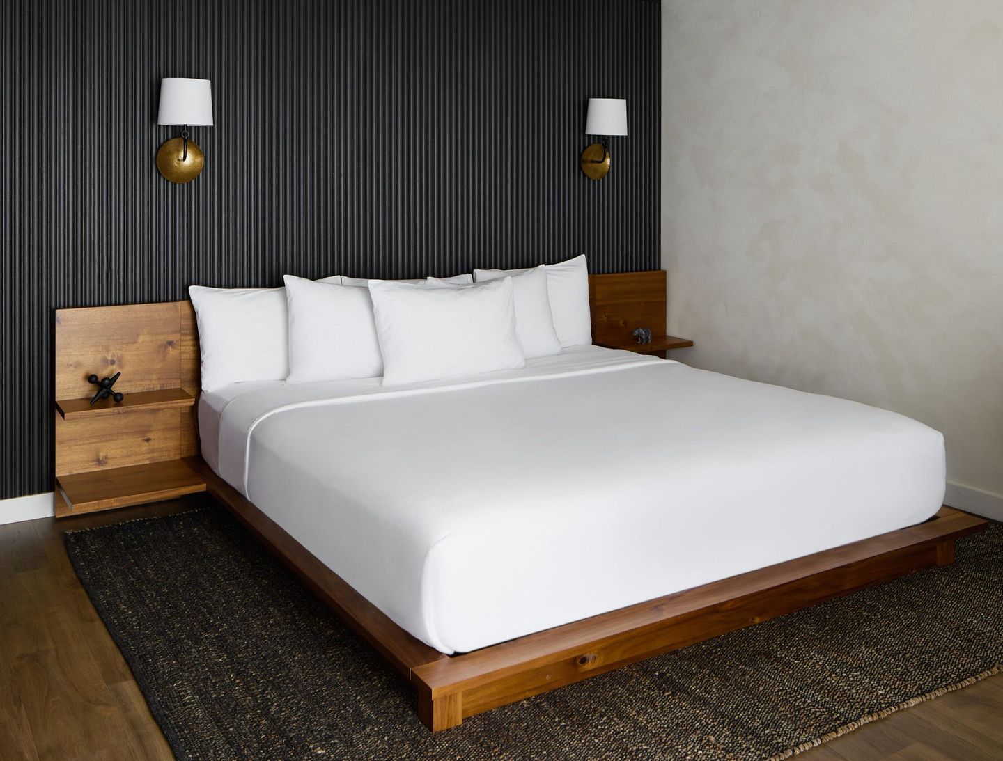 Modern hotel room with a wooden bed, white bedding, dark curtains, and wall lamps
