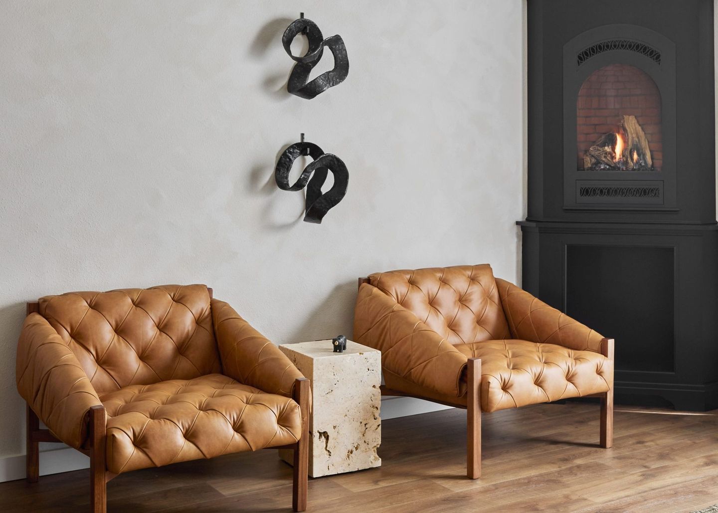 Two tan leather chairs beside a small marble table in a cozy room with a fireplace