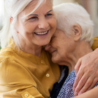 Deux femmes âgées se serrent dans les bras et sourient.
