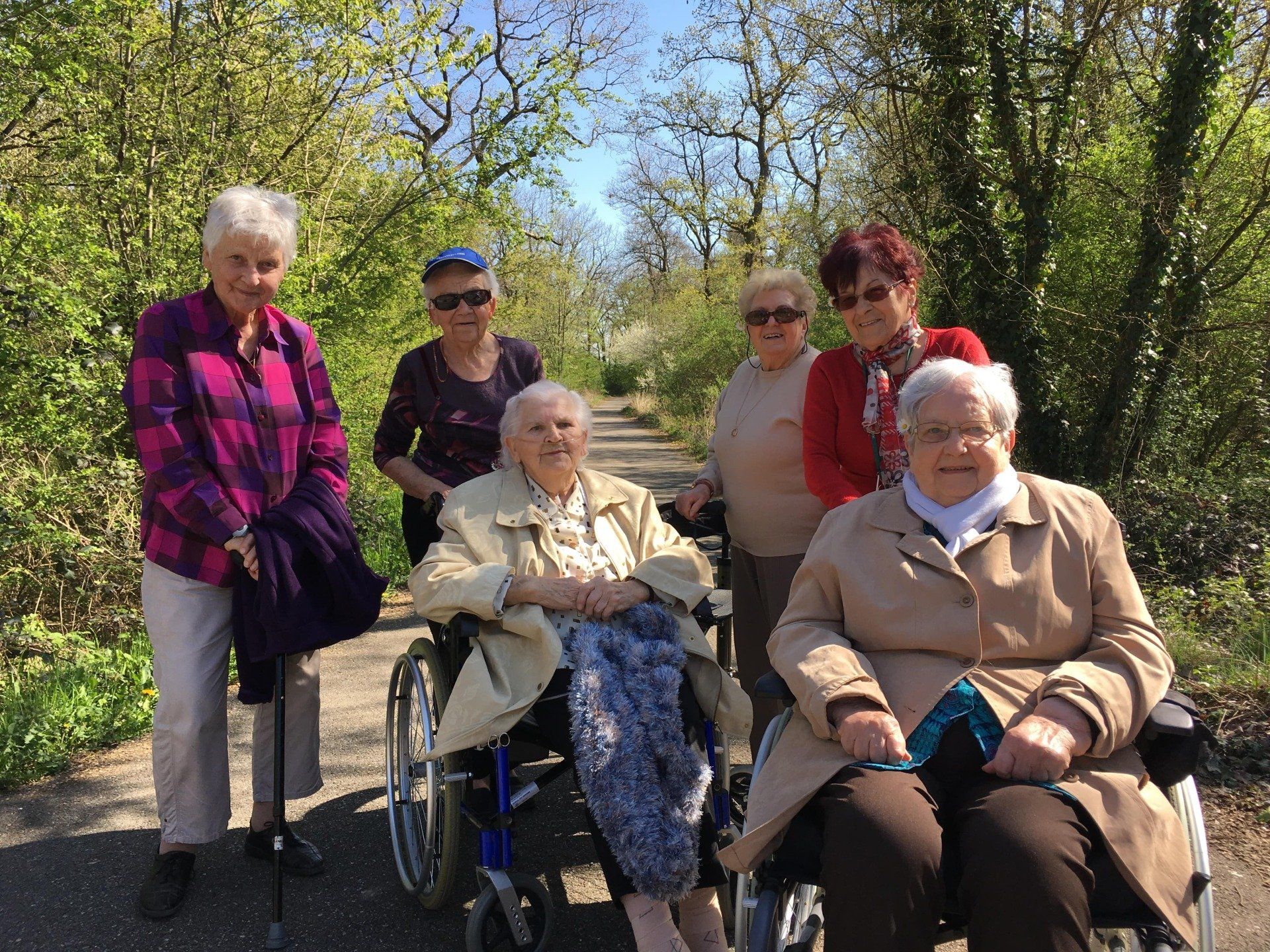 Un groupe de femmes âgées en fauteuil roulant se tiennent côte à côte sur un chemin.