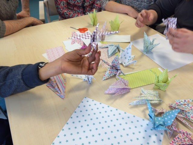 Un groupe de personnes est assis autour d'une table et fait des oiseaux en origami