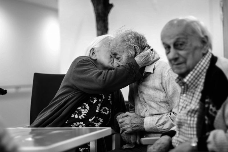 Deux personnes âgées se serrent dans les bras sur une photo en noir et blanc.