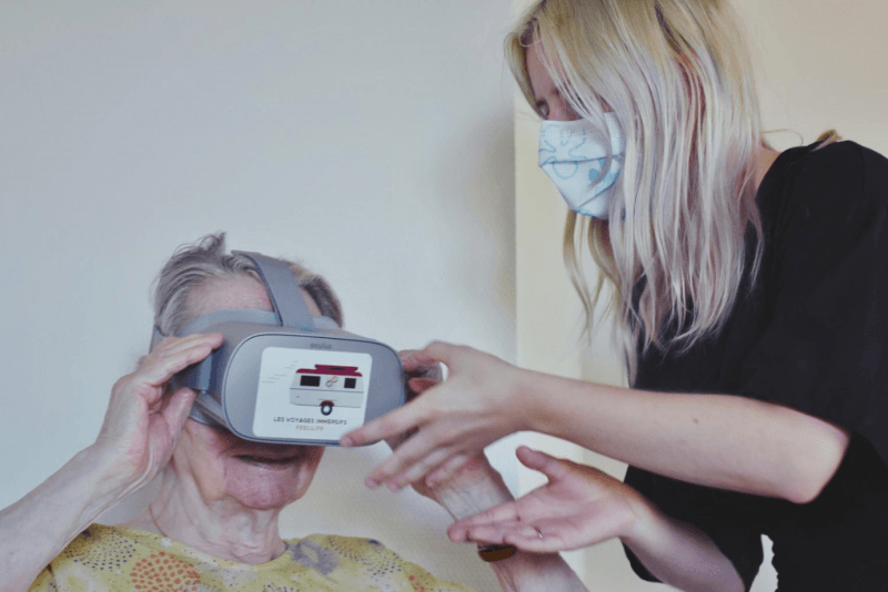 Une femme portant un masque aide une femme âgée à porter un casque de réalité virtuelle.