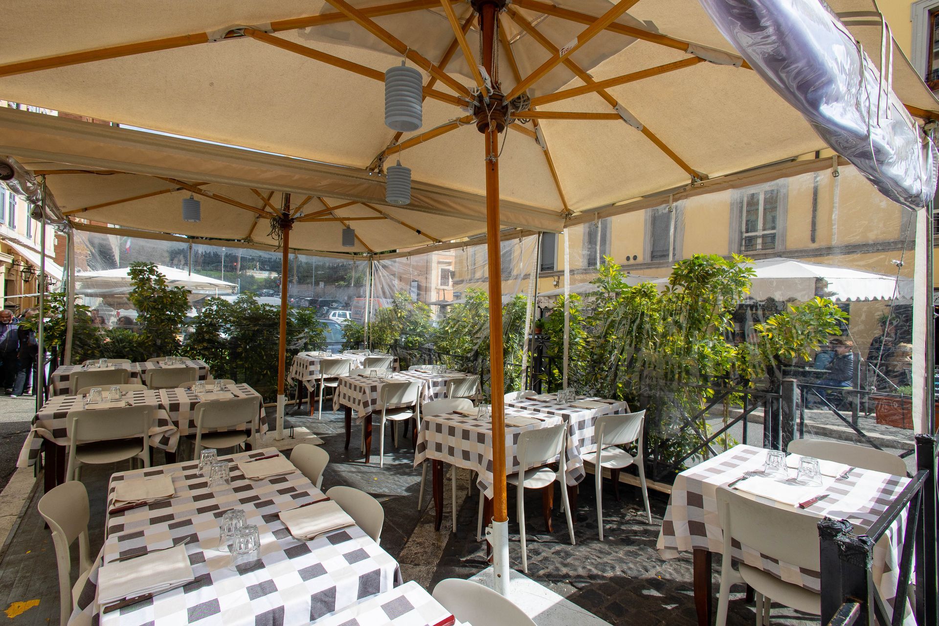 Tavolini all'aperto in un cortile soleggiato, sotto ombrelloni beige, con tavoli e sedie bianche.