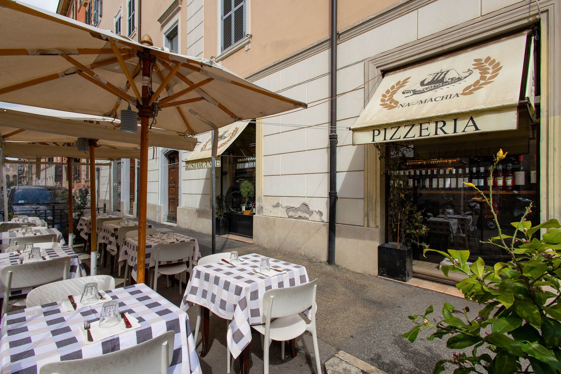 Pizzeria all'aperto con tavolini bianchi e ombrelloni lungo una stradina in una soleggiata cittadina in stile italiano.
