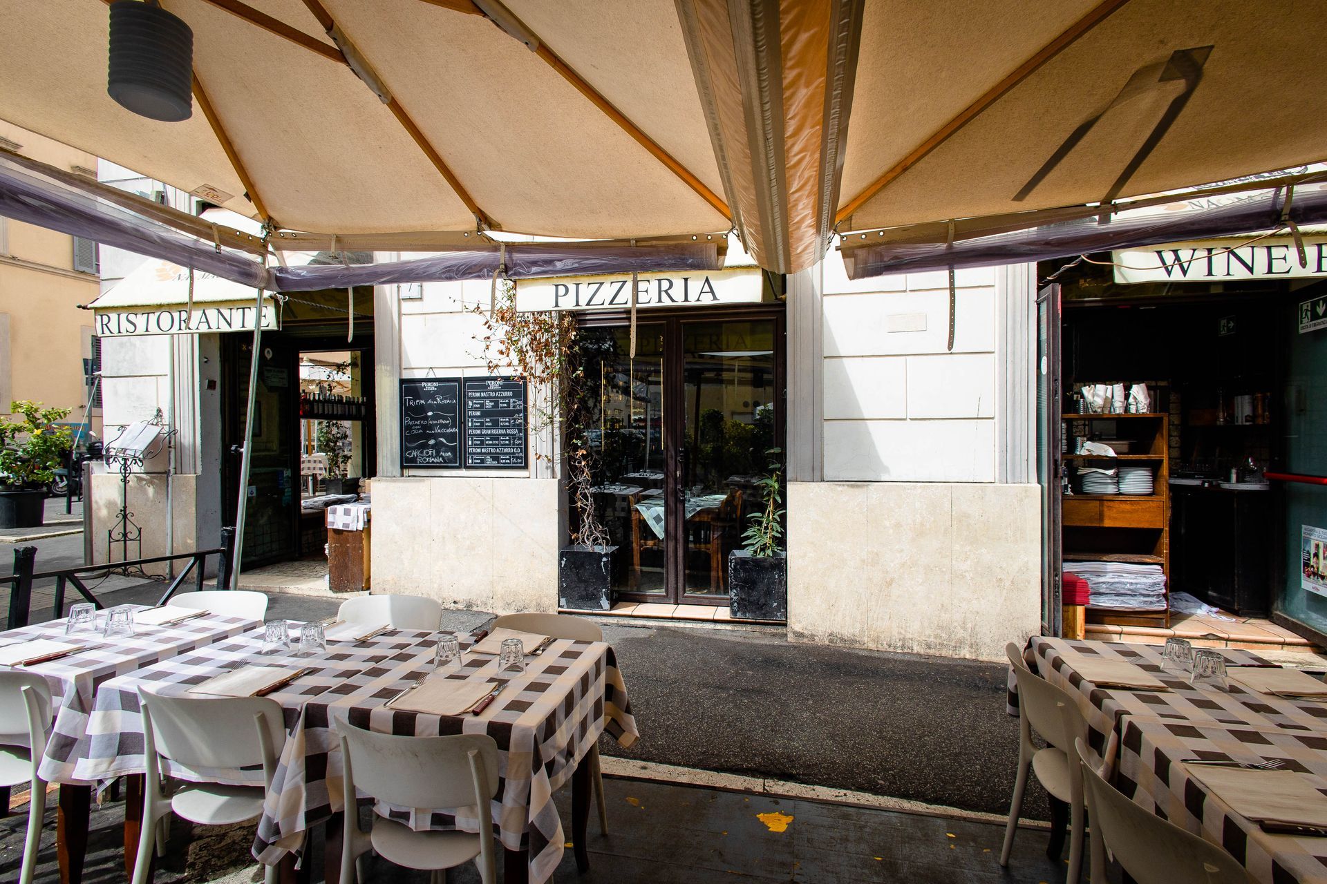 Tavolini all'aperto sotto ombrelloni color beige di fronte alla vetrina di un'enoteca.