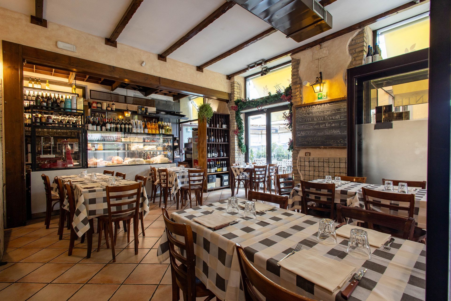 Accogliente interno del ristorante con tavoli in legno, tovaglie a quadri, scaffali da bar e luci calde.