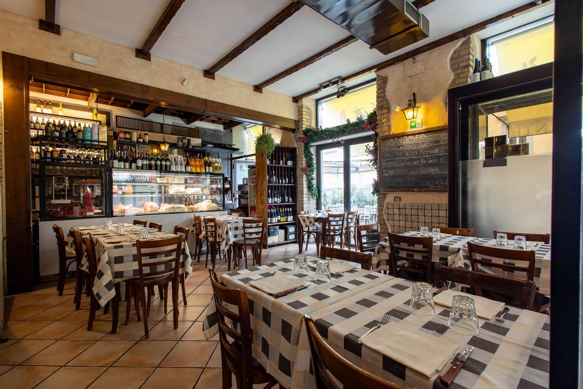 Accogliente interno del ristorante con tavoli in legno, tovaglie a quadri e un bancone bar pieno di bottiglie.