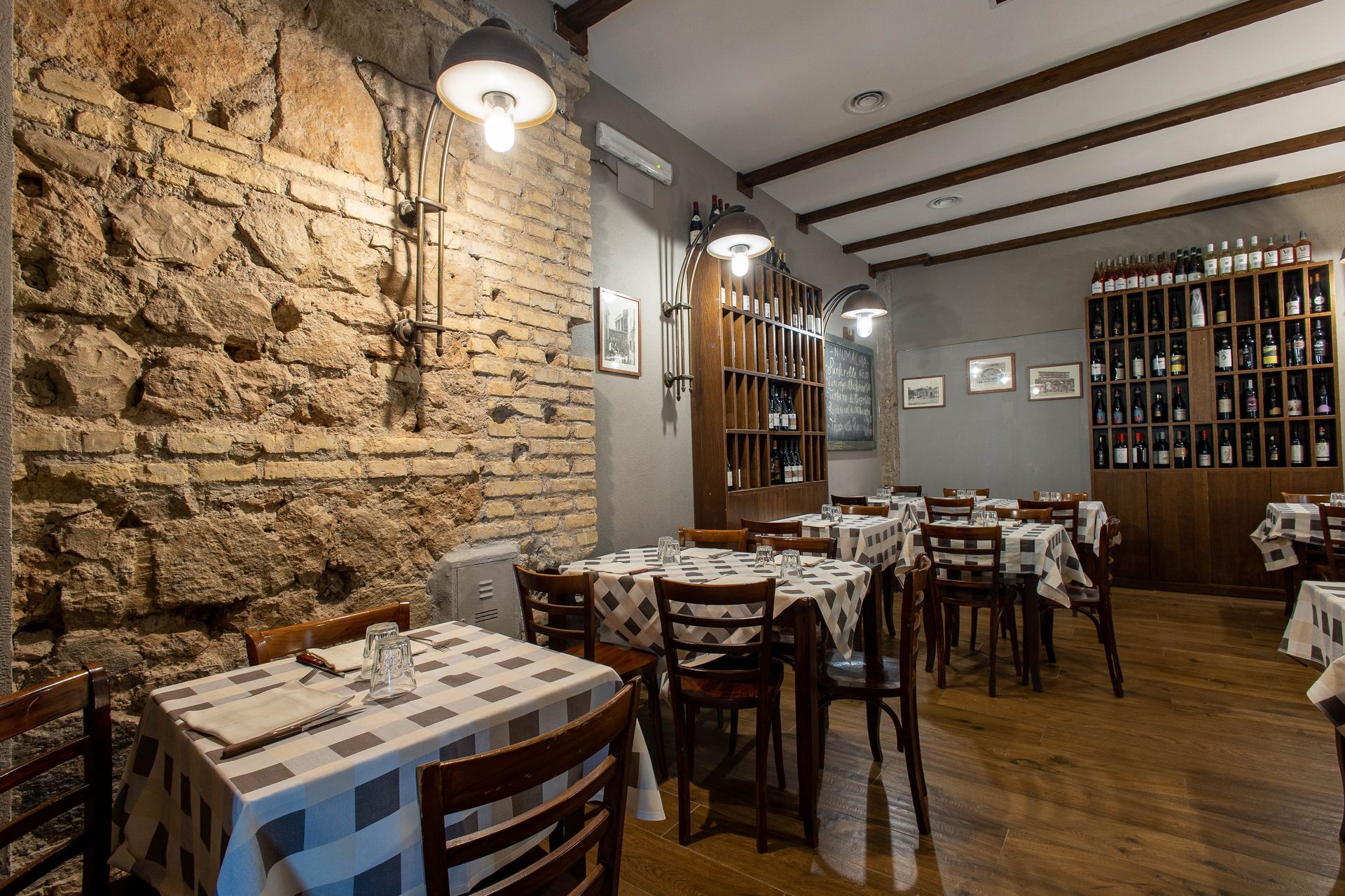 Accogliente interno rustico di un ristorante con parete in pietra, tavoli e sedie in legno e portabottiglie sulla parete di fondo.