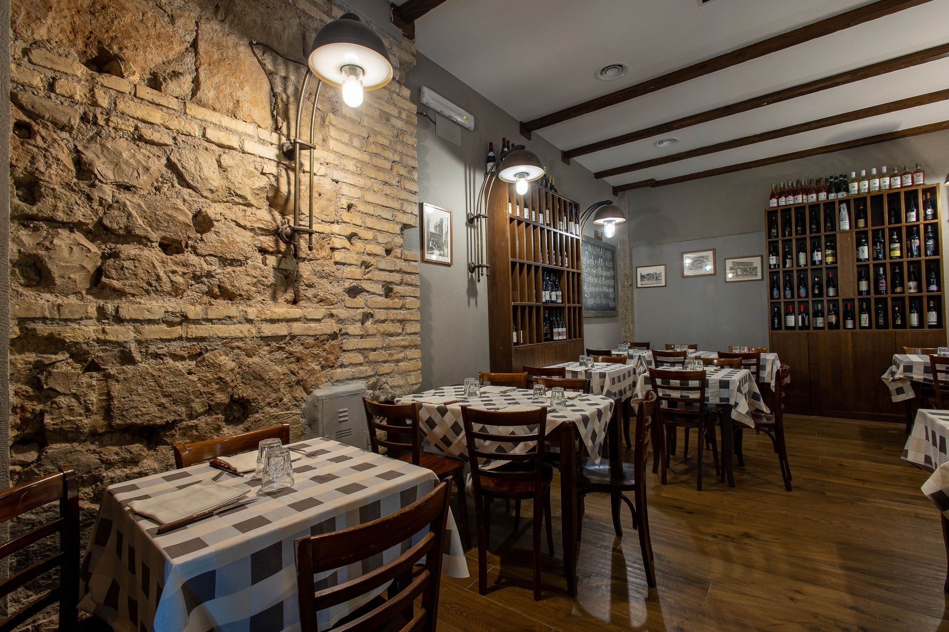 Accogliente sala da pranzo in stile rustico con parete in pietra, tavoli in legno e scaffali portabottiglie.
