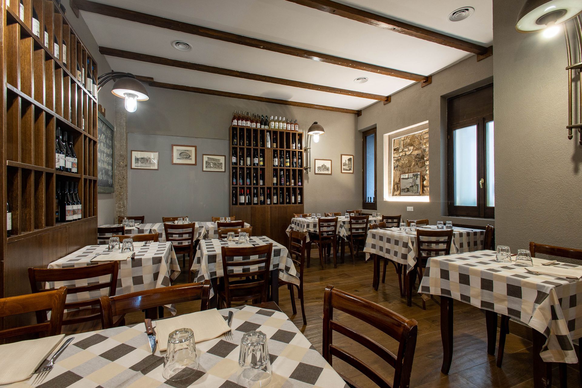 Sala da pranzo vuota di un ristorante con sedie di legno, tovaglie a quadri e mensole a muro.