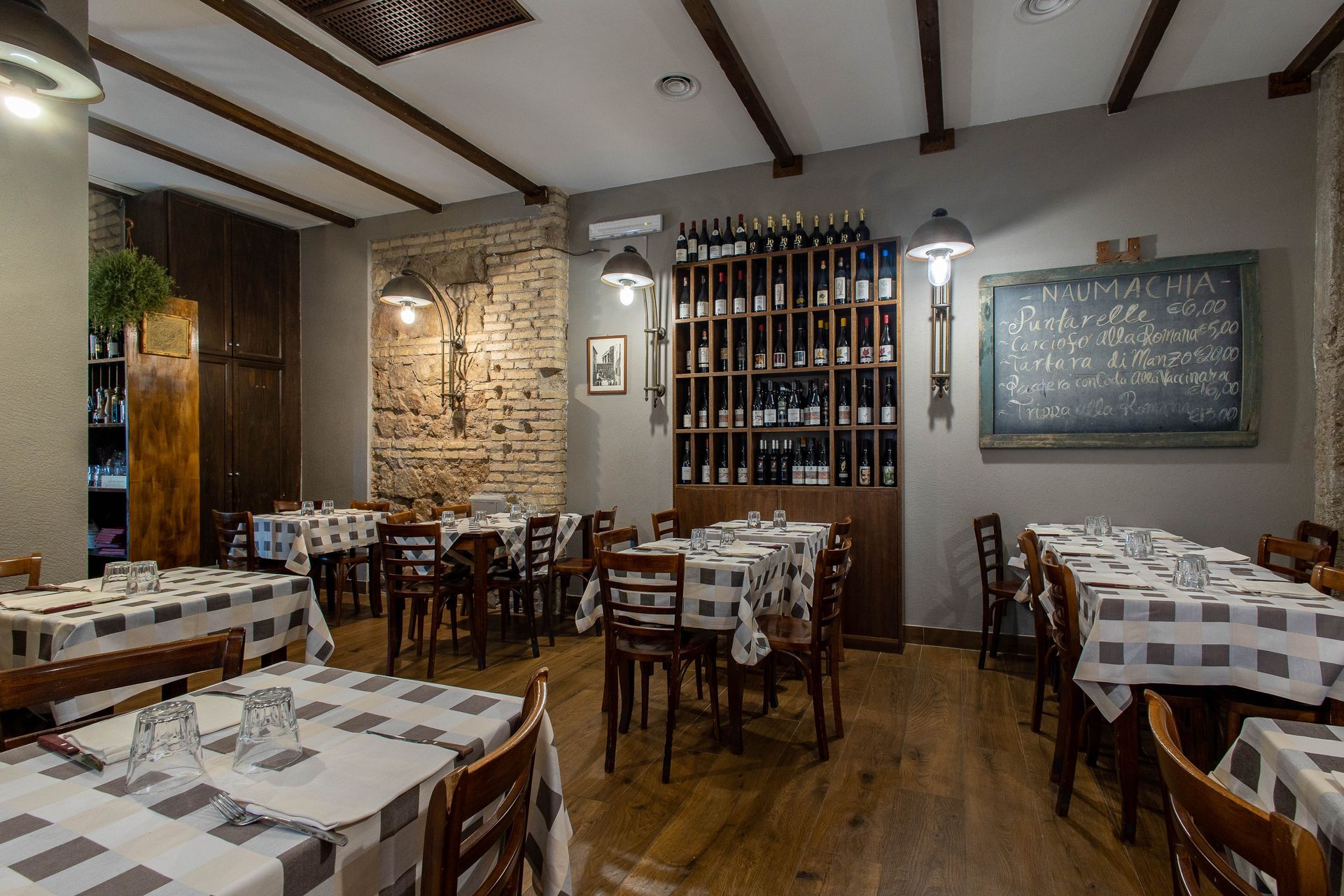 Sala da pranzo vuota di un ristorante rustico con tavoli a scacchi, sedie in legno, travi a vista e una rastrelliera per il vino.