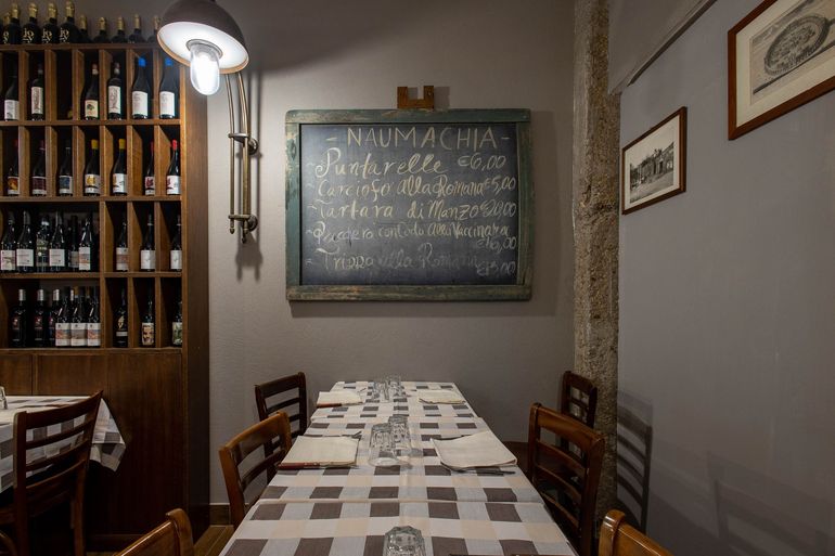 Accogliente sala da pranzo del ristorante con tovaglie a quadri, portabottiglie e una lavagna con il menù appeso alla parete.