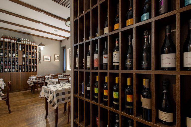 Bottiglie di vino esposte su scaffali in un'accogliente sala da pranzo di un ristorante con tavoli a scacchi