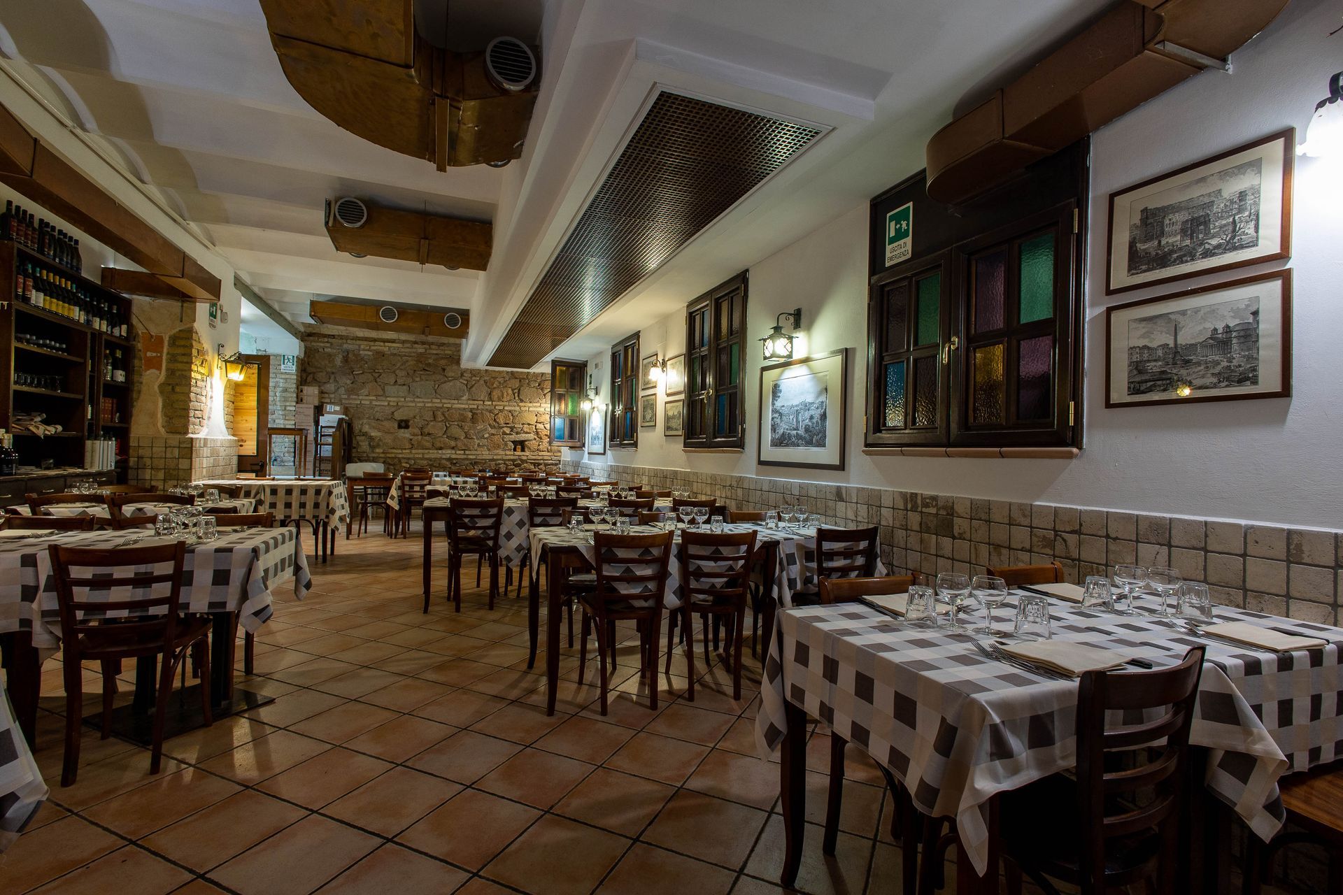 Sala da pranzo vuota di un ristorante rustico con tovaglie a quadri e luci calde.