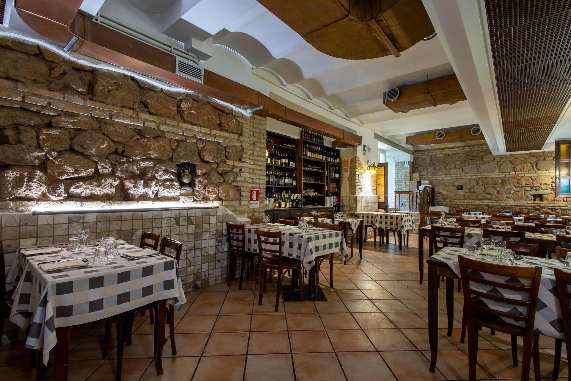 Ristorante rustico con pareti in pietra, tavoli a scacchi, sedie in legno e luci calde.