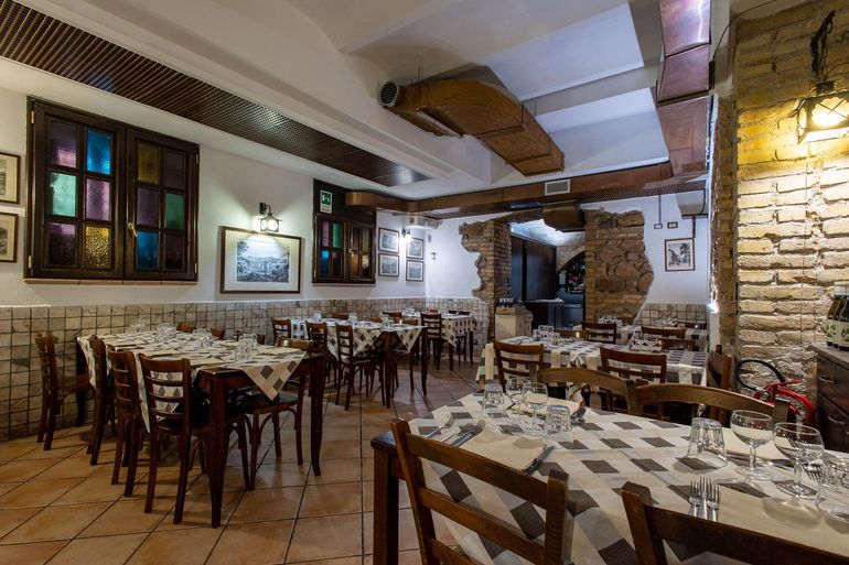 Accogliente sala da pranzo in stile rustico con tavoli in legno, tovaglie a quadri e calde applique a parete.