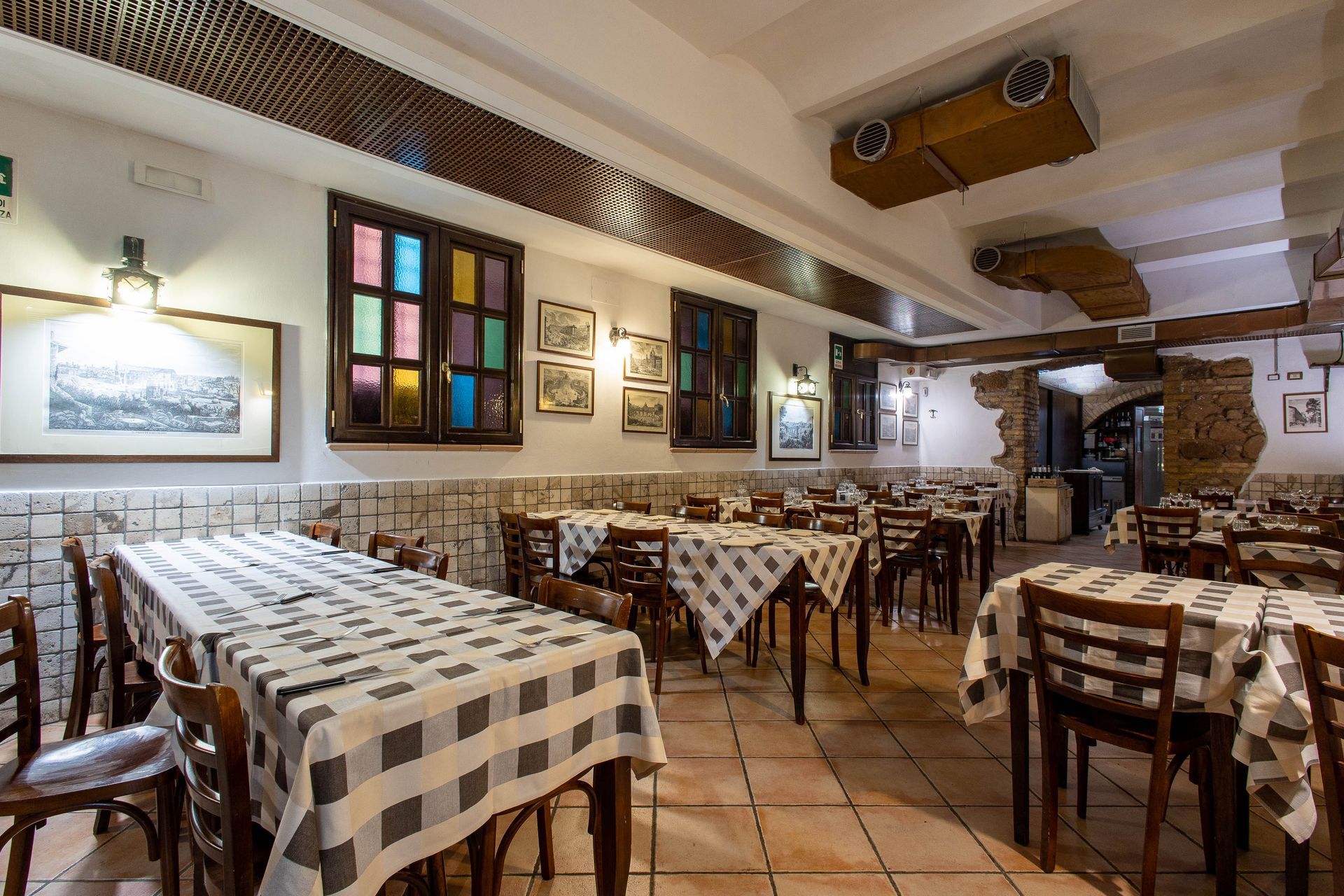 Accogliente sala da pranzo in stile rustico con tovaglie a quadri, sedie in legno e quadri appesi alle pareti.