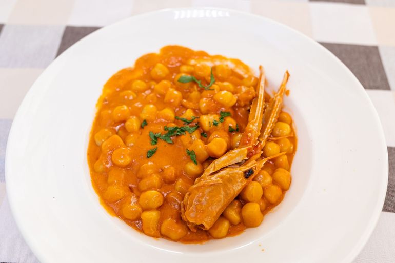 Piatto bianco con stufato di ceci all'arancia, erbe aromatiche e guarnizione di chela di granchio, su una tovaglia a quadri.