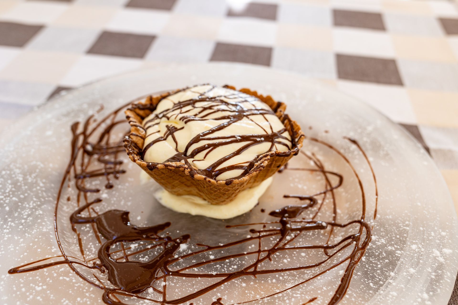 Crostata dolce con gelato alla vaniglia e glassa al cioccolato, servita su un piatto cosparso di zucchero a velo.