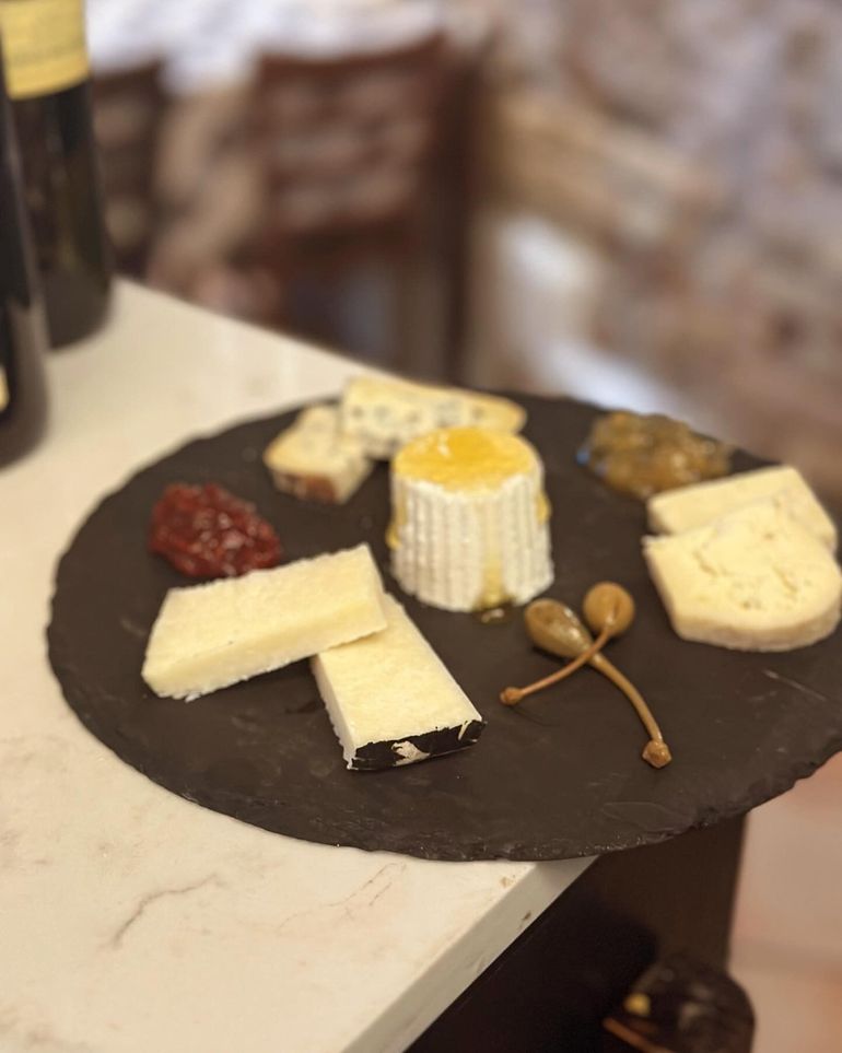 Piatto di formaggi su un tagliere rotondo scuro con formaggi assortiti, marmellata e cucchiaino per il miele su un tavolo