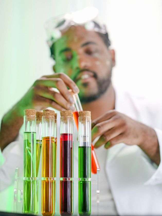 Een persoon in een laboratoriumjas en met een veiligheidsbril op werkt in een laboratorium met kleurrijke reageerbuizen