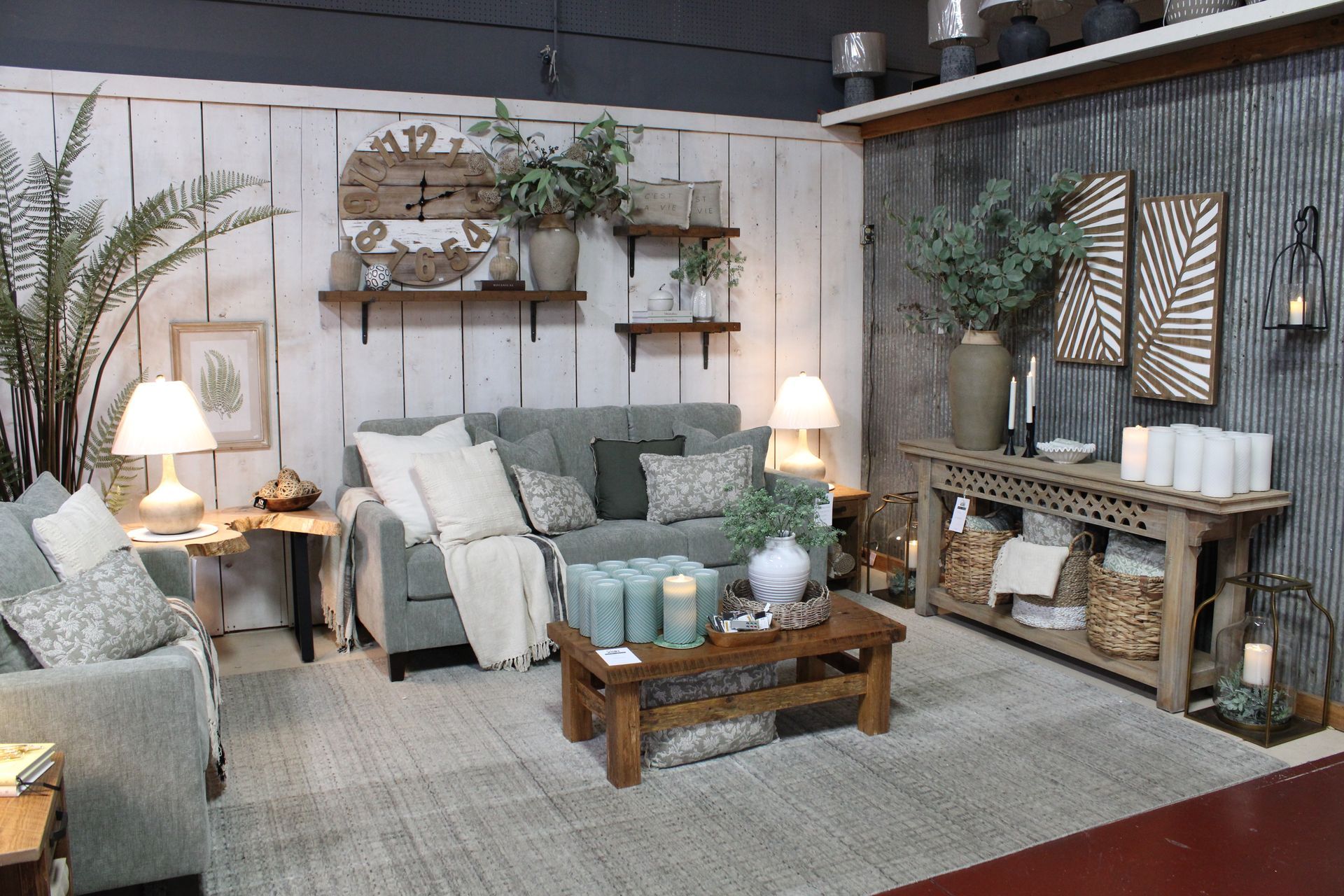 Cozy living room display with sofas, tables, rug, art, and decor against a wood-paneled wall and string lights.