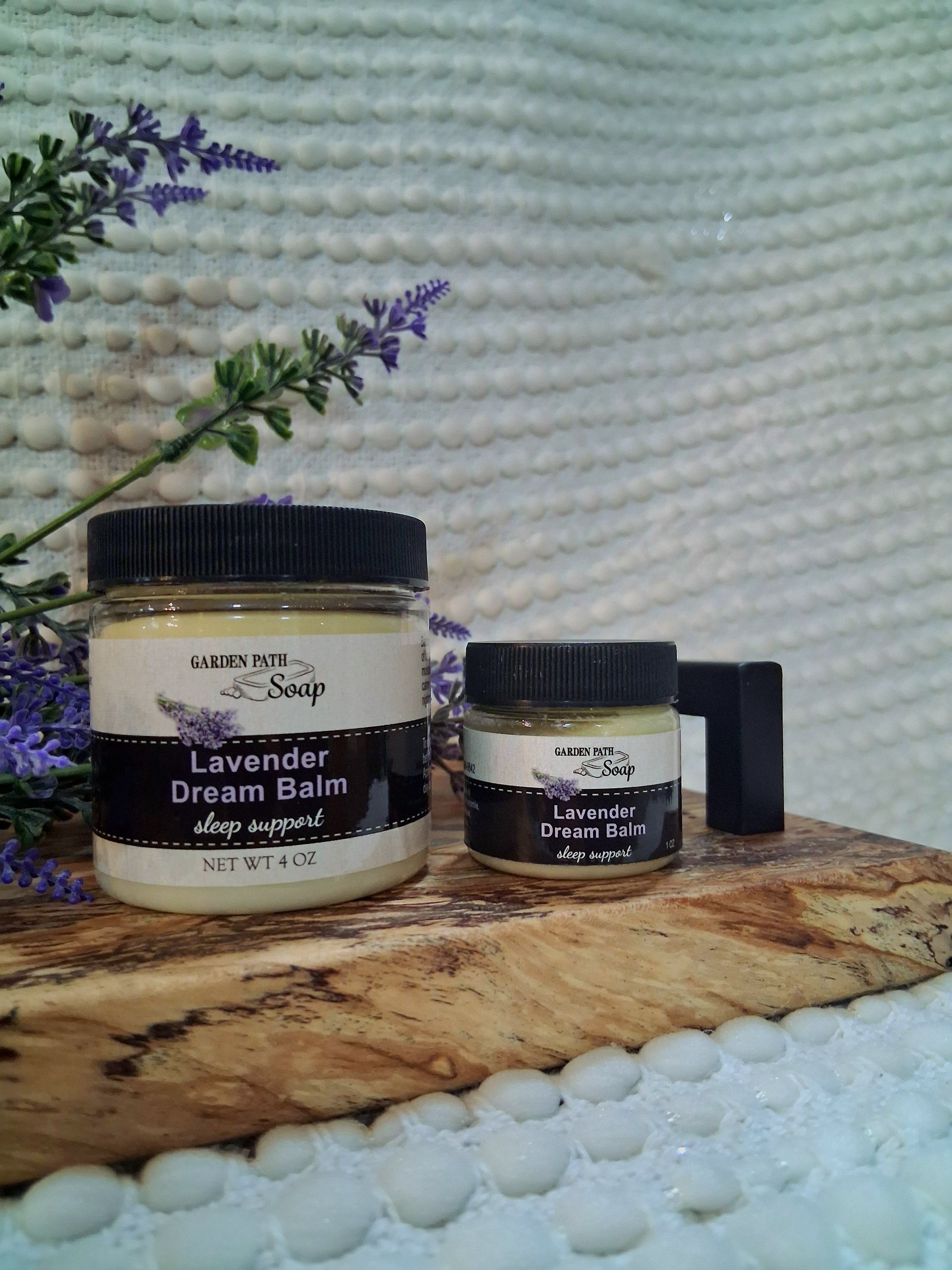 Two jars of lavender dream balm on a wooden board with lavender sprigs.