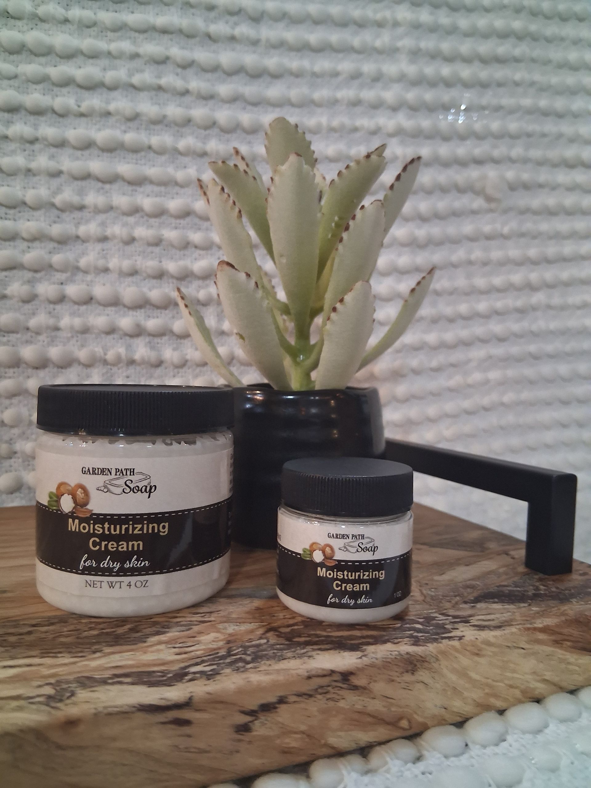 Two jars of moisturizing cream, a plant, and a black handle on a wooden board.