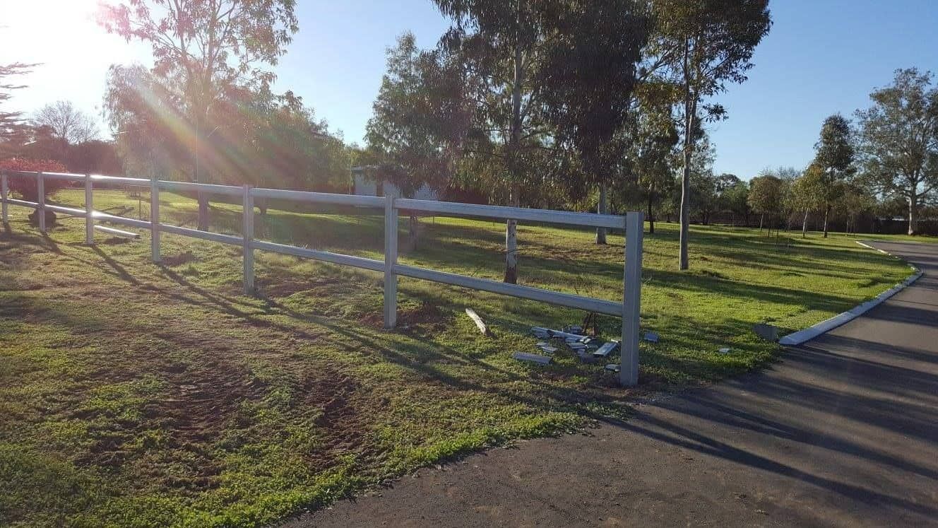 A White Fence Surrounds A Grassy Field Next To A Road — Anne & Ron Johnson Fencing in Werris Creek, NSW