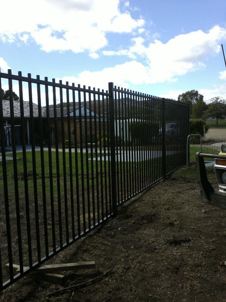 A Man Is Working On A Metal Fence In A Park — Anne & Ron Johnson Fencing in Werris Creek, NSW