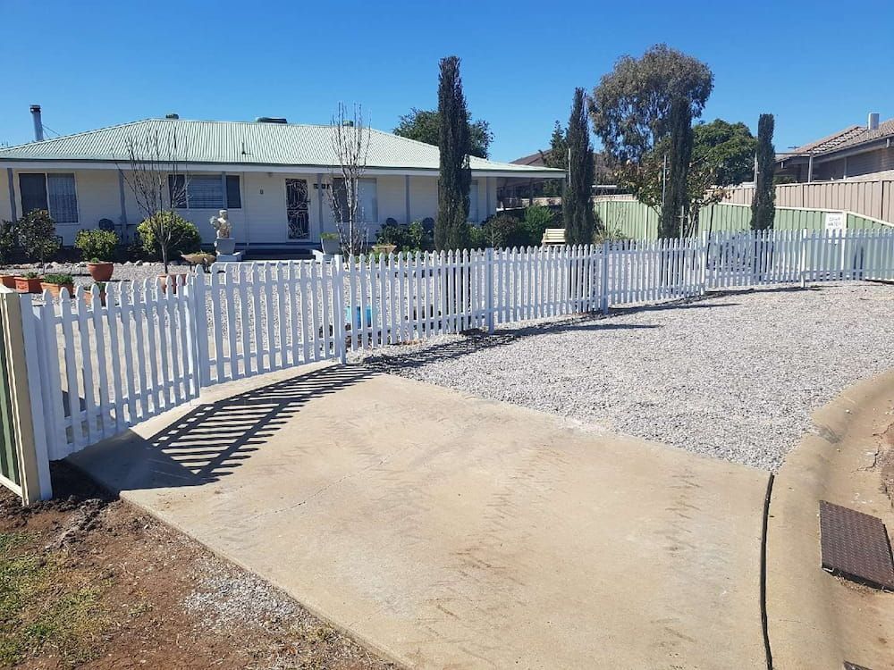 A White Picket Fence Surrounds A Gravel Driveway In Front Of A House — Anne & Ron Johnson Fencing in Werris Creek, NSW