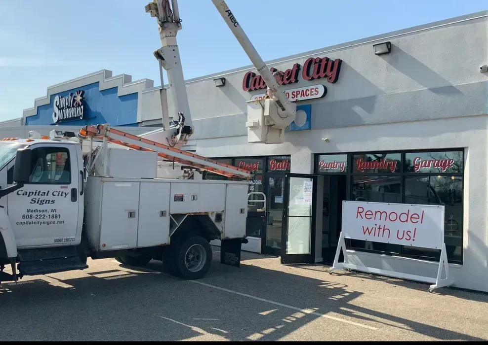 Utility truck outside a storefront with a “Remodel with us!” banner and a lift basket raised overhead