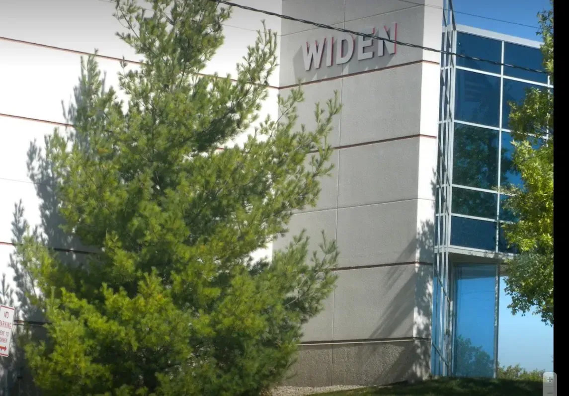 Office building with glass windows and the word “WIDEX,” partly hidden by trees
