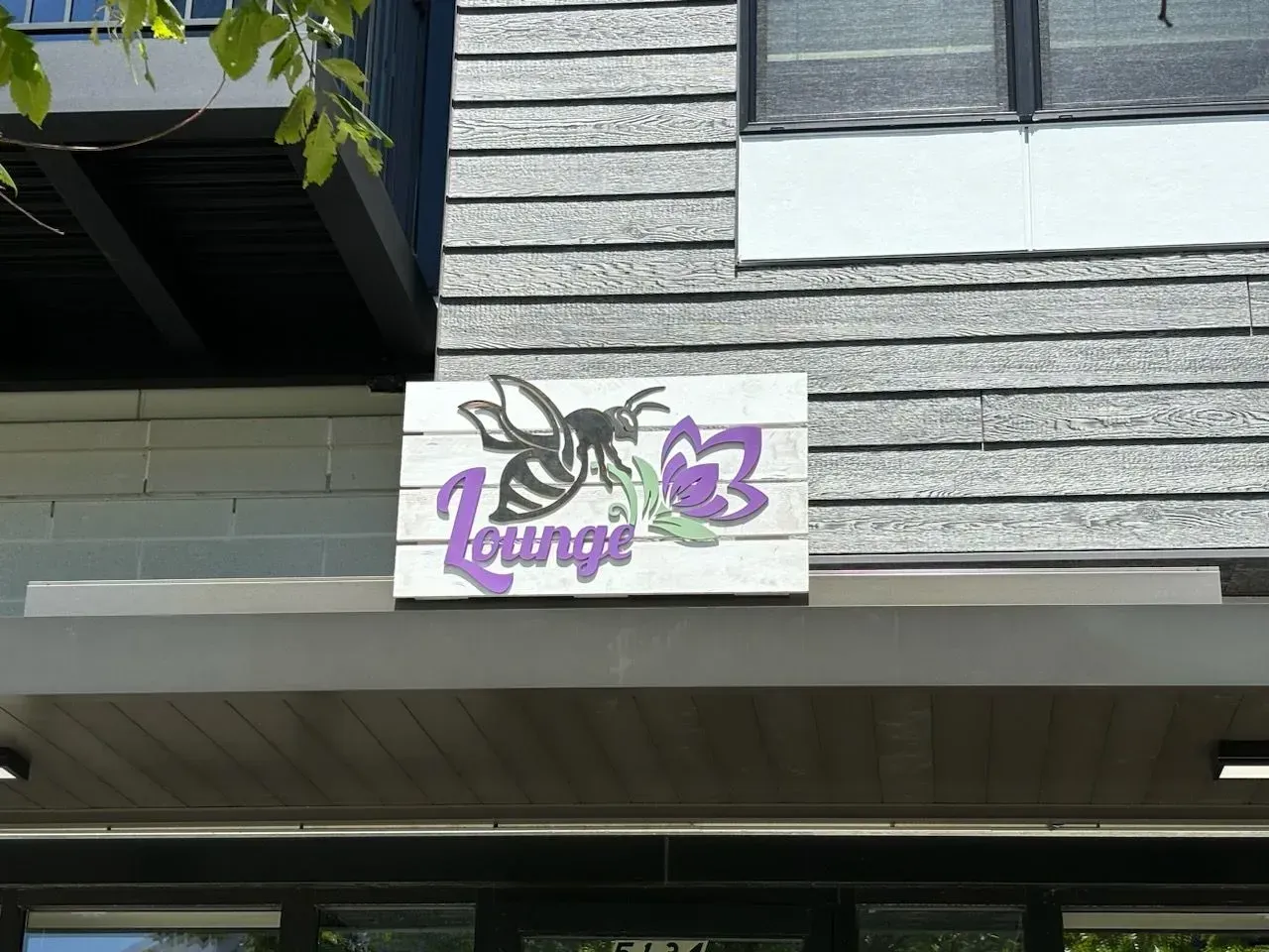Purple-and-white “lounge” sign on a gray building exterior.