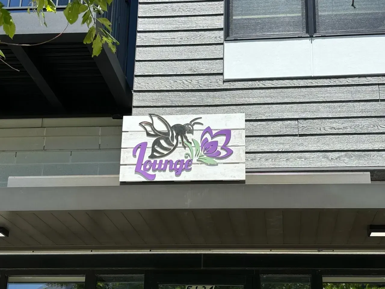 White “lounge” sign with purple butterfly logo on a gray shingle building.