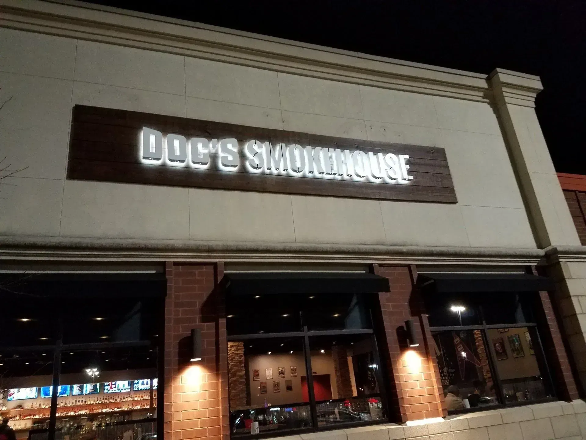 Lit storefront sign reading “Joe’s Smokehouse” on a brick-and-stucco building at night