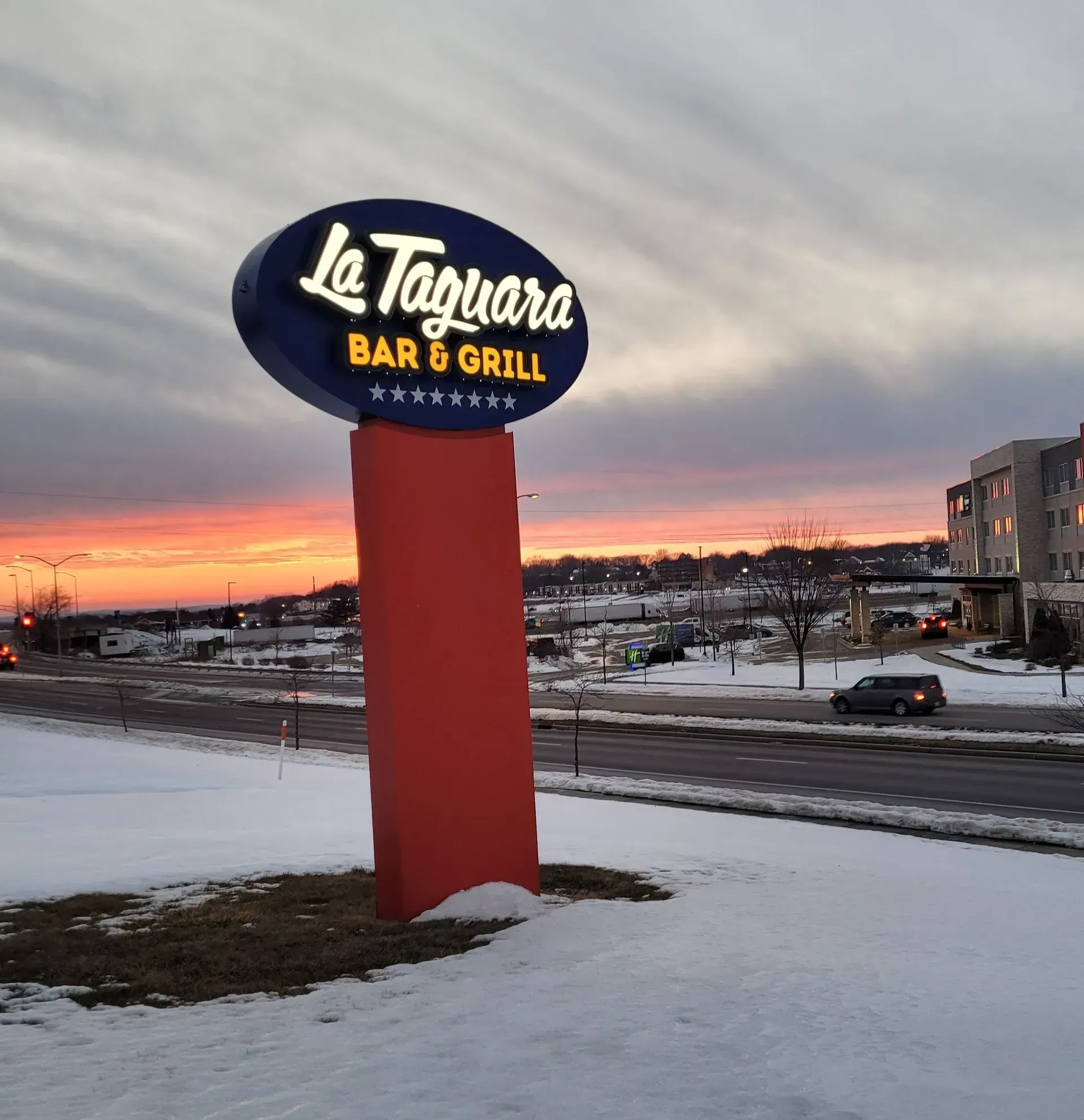 Le Teguire Bar & Grill sign at dusk above a snowy roadside with sunset sky
