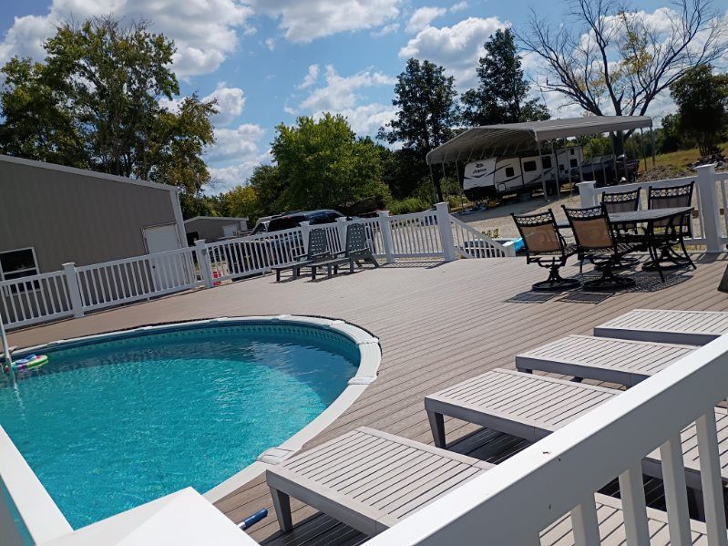 Swimming pool with white lounge chairs and patio tables on a sunny deck under a partly cloudy sky