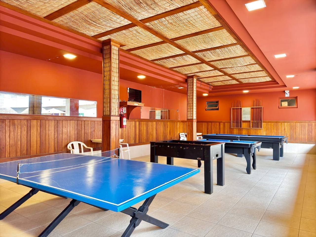 Sala de recreação interna com mesa de pingue-pongue azul, mesas de pebolim e paredes laranja