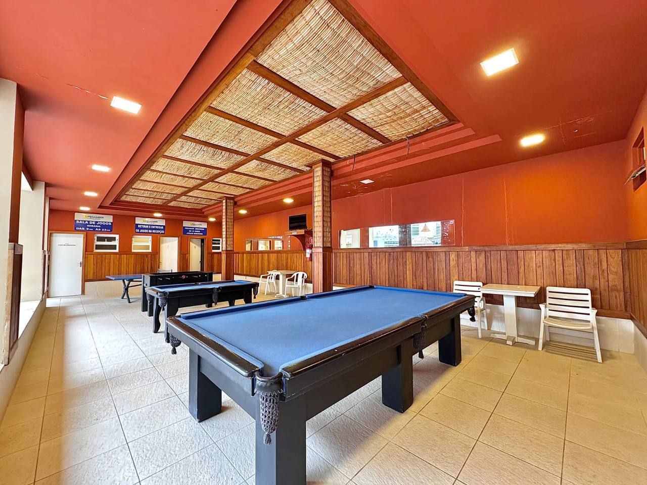 Salão de bilhar coberto, com mesas de feltro azul sob um teto vermelho e iluminação acolhedora