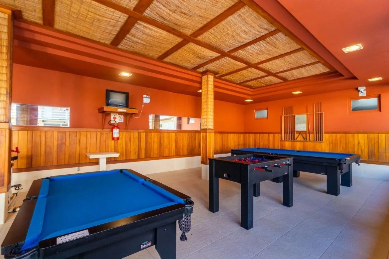 Sala de jogos com mesas de bilhar e de hóquei de mesa, paredes laranja e teto de palha trançada
